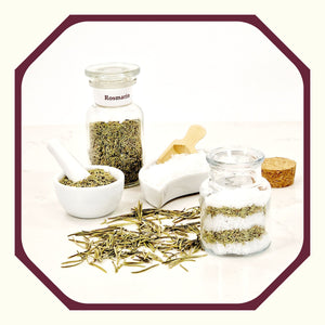 Rosmarin im Glas neben einem kleinen weißen Mörser, gefüllt Rosmarin, einer kleinen weißen Schale mit Fleur-de-Sel und einer Salzschaufel, einem Glas mit Rosmarin-Gourmet-Salz, Rosmarinnadeln