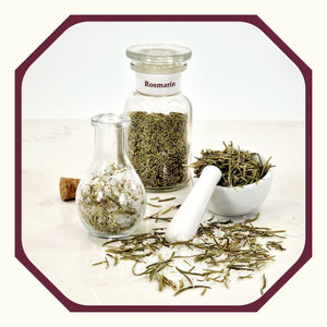 Rosmarin im Glas neben einem Glas mit Rosmarin-Peeling-Salz, einem kleinen weißen Mörser mit Rosmarinnadeln und Rosmarin und Salz