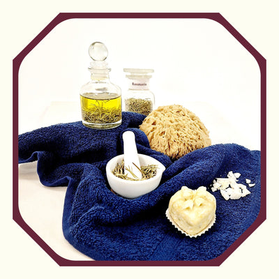 Rosmarin im Glas auf einem blauen Handtuch, daneben eine Flasche Rosmarin-Mandelöl, ein Naturschwamm, ein kleiner weißer Mörser mit Rosmarin, eine kleine Seife in Herzform, ein paar Seifenstücke, geraspelt