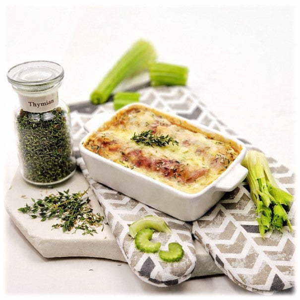 Thymian im Glas, davor Thymian-Kräuter, auf einem Küchenhandschuh eine kleine Auflaufform mit überbackenem Staudensellerie, daneben einige Stücke Stangensellerie geschnitten