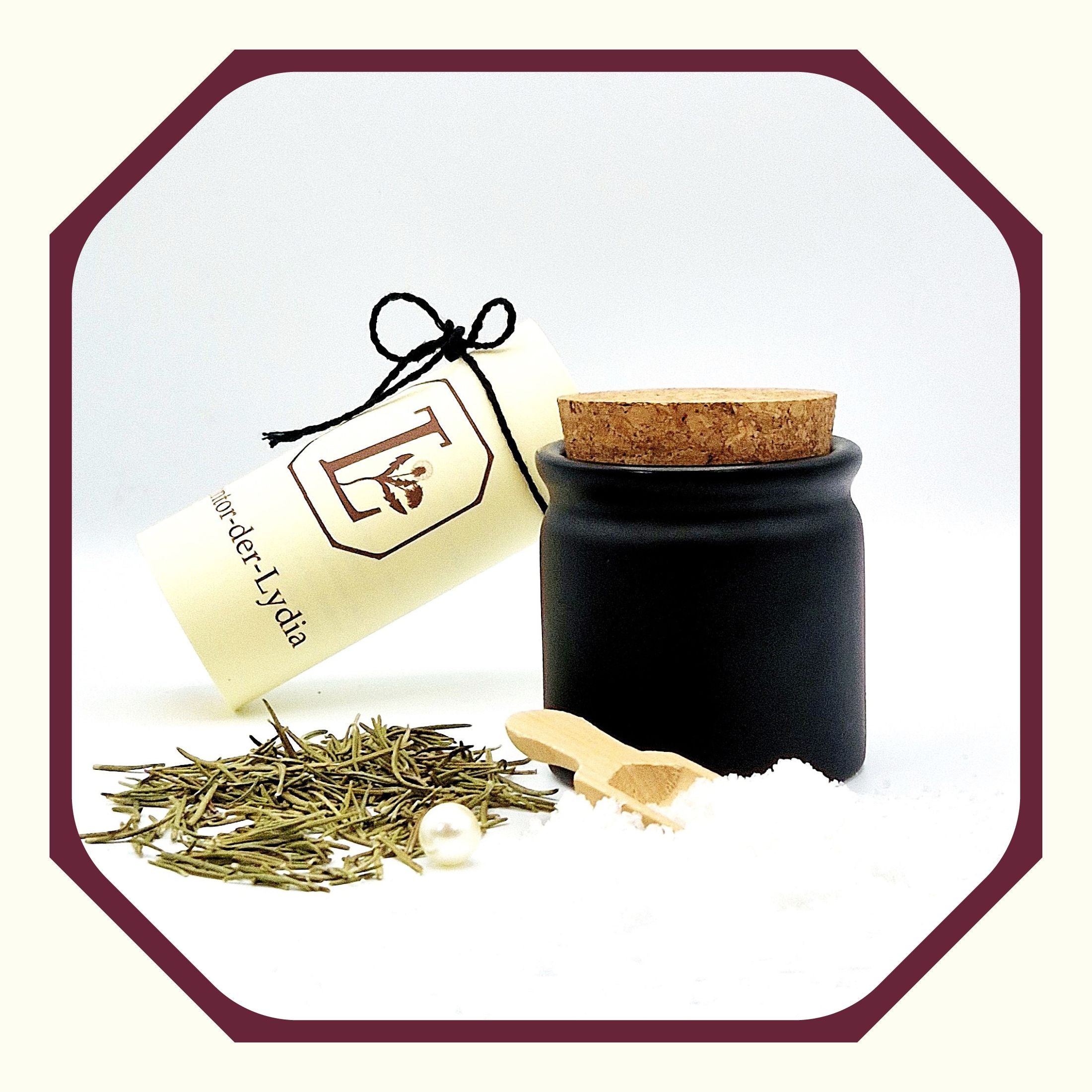 Eine Perle, eine rund gefaltete Karte mit schwarzem Schleifenband, ein schwarzer Salztopf oder Kräutertopf aus Keramik, davor Salz Fleur-de-Sel, Rosmarin, eine kleine Salzschaufel aus Holz