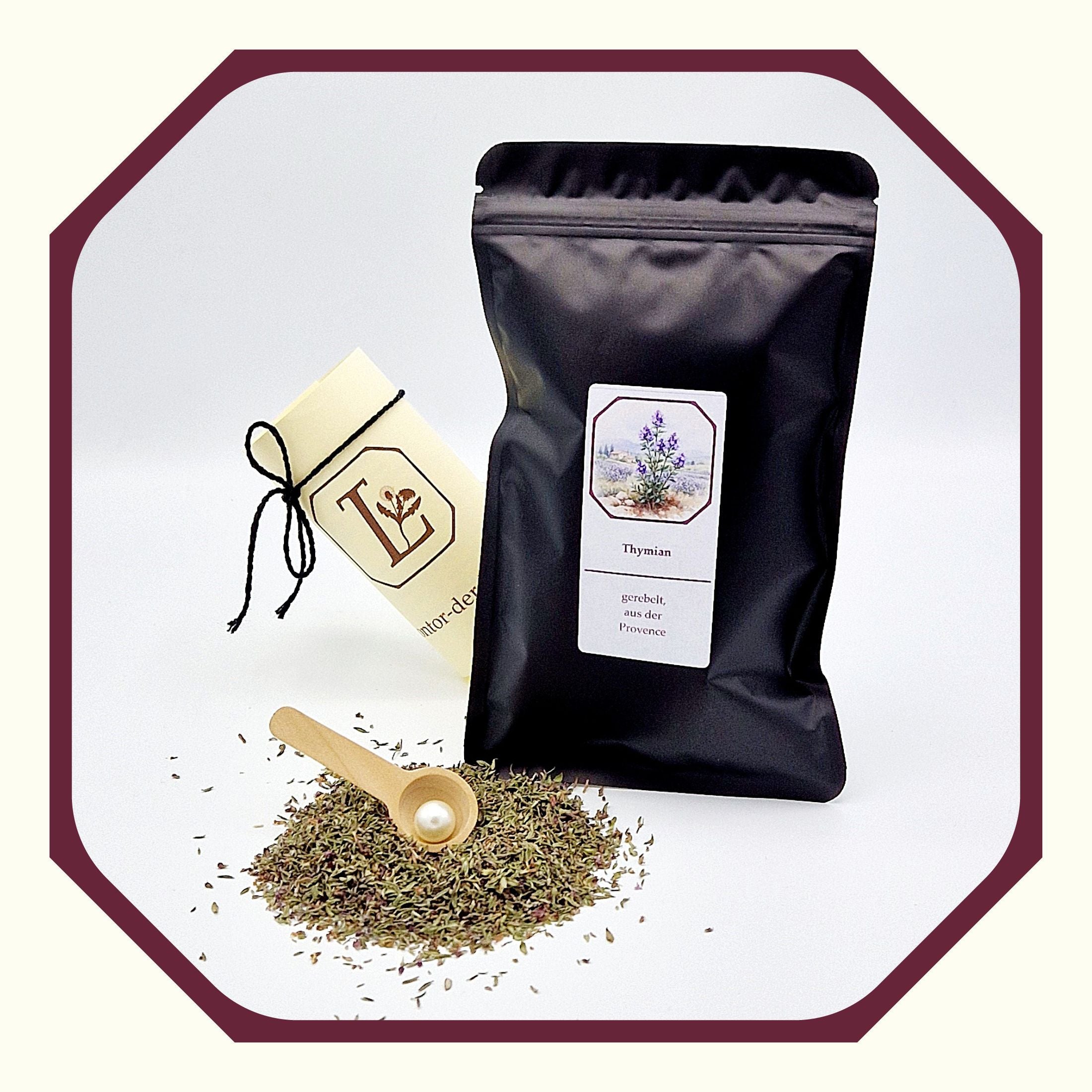 Eine Perle in einem Kräuter-Löffel, eine rund gefaltete Karte mit schwarzem Schleifenband, ein schwarzer Beutel gefüllt mit Thymian aus der Provence, loser Thymian vor dem Beutel